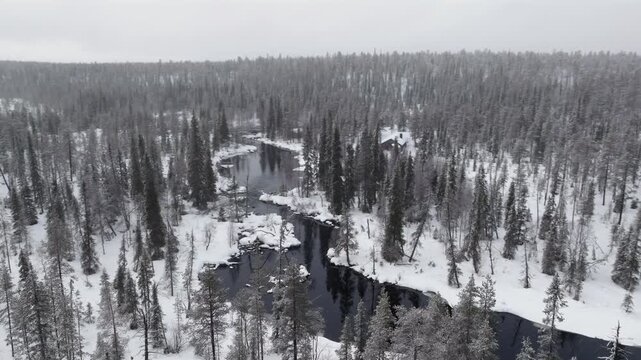 Aerial, orbiting towards a river surrounded by snow-covered forest while it's snowing