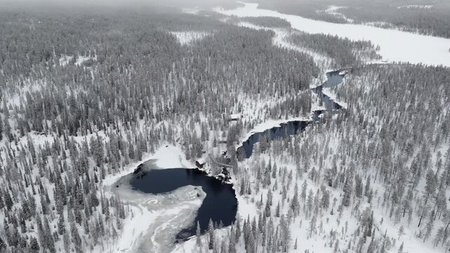 Aerial, slowly orbiting high above a river surrounded by snow-covered forest