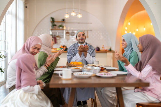 Muslim family praying before eating iftar meal during ramadan or eid together around dining table, tradition faith gratitude love, islamic culture peaceful moment with food and family, halal food - Powered by Adobe