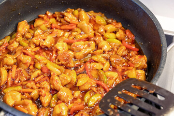 A close-up shot of sweet and sour chicken stir-fried in a pan with peppers and other vegetables, ready to be served