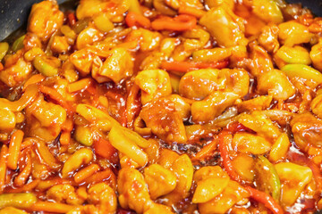 A close-up shot of a vibrant sweet and sour stir-fry with colorful peppers and juicy chicken pieces in a glossy sauce