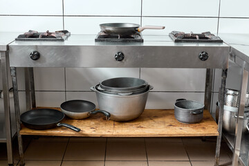 Industrial kitchen with gas stove and metal cookware on wooden storage shelf