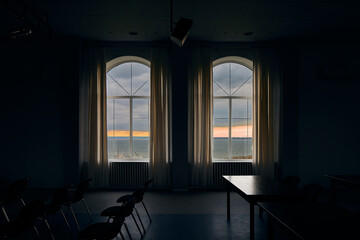 Dark room with chairs and tables, large windows overlooking sunset lake
