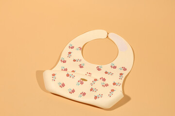 Cream floral silicone baby bib;  soft, pastel colors;  modern design;  clean background.