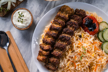 Top view of grilled beef kebab with colorful basmati rice, roasted tomato, cucumber slices, yogurt...