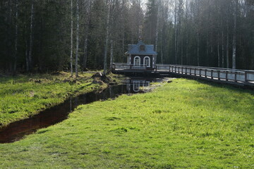 narrow river between banks with green grass and wooden house in the background