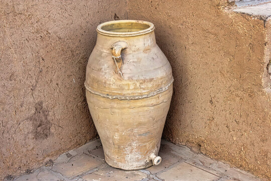 A large, old, and dirty vase sits on a corner of a wall
