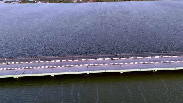 Wide-angle aerial view of the modern Kadalur Bridge gracefully crossing expansive water in Chennai, connecting land with distant, lush marshlands under a soft sky. Palar River flowing to Sea
