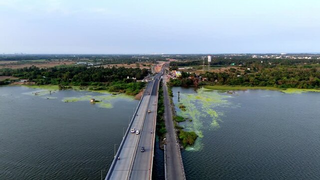 Drone shot capturing a vital road bridge over a lake in Chennai, showing light traffic and lush green surroundings extending to the horizon. accented by natural green aquatic growth
