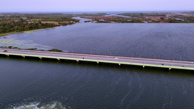 Aerial view over Chennai's coastal landscape, featuring a long bridge spanning wide backwaters where vibrant green algae islands create a stunning contrast, leading to distant wetlands. Bay of Bengal