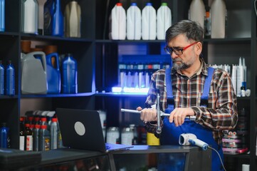 Salesman holding car part and looking at laptop in auto parts store