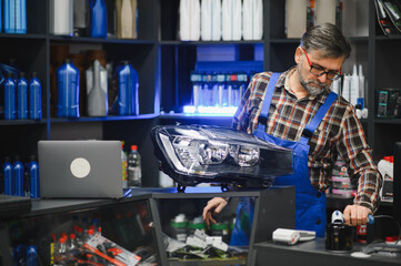 Salesman holding car headlight and picking oil filter in auto parts store