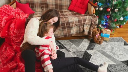 Happy family having fun at home for Christmas. Mother tickles her daughter sitting on the floor. Festive cozy interior - Powered by Adobe