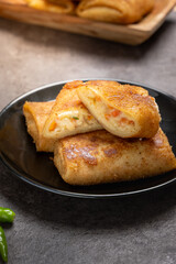 Close-up of Indonesian risoles filled with vegetables and mayonnaise, stacked on a black plate with stone surface background, showing golden crispy texture and savory filling in natural light