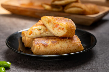 Close-up of Indonesian risoles filled with vegetables and mayonnaise, stacked on a black plate with stone surface background, showing golden crispy texture and savory filling in natural light