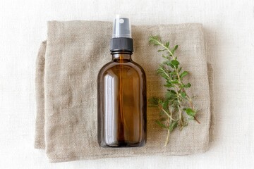 Fototapeta premium Amber spray bottle on linen cloth with herbs