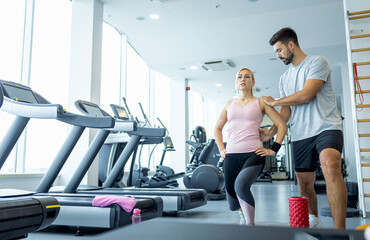 Personal fitness trainer supervising middle aged woman during gym workout.