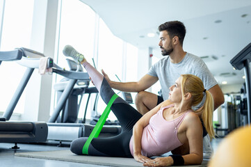 Personal fitness trainer supervising middle aged woman during gym workout.