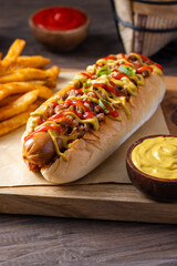 Close-up of juicy hot dogs topped with ground meat, mustard, ketchup, and green onions on soft buns, served on brown paper with mustard dip and rustic wooden background in natural lighting