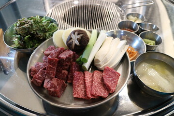 Korean Barbecue Grill Setup with Fresh Beef, Side Dishes, and Vegetables at Traditional Restaurant Table
