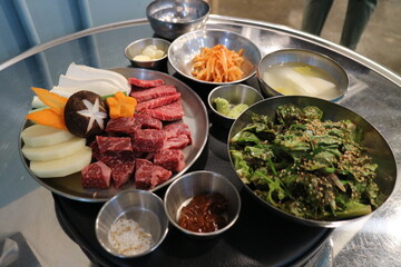 Korean Barbecue Grill Setup with Fresh Beef, Side Dishes, and Vegetables at Traditional Restaurant Table
