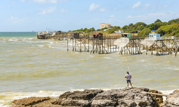pecheur &agrave; la ligne sur le bord du littoral de l'ocean atlantique face a des cabanes de p&ecirc;che au carrelet a Saint Palais sur Mer, region Nouvelle-Aquitaine
