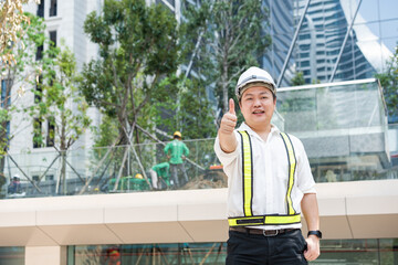With a bright smile and a thumbs up a smiling Asian construction professional acknowledges success...