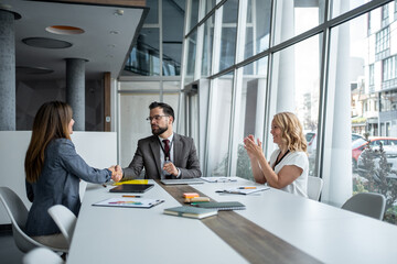 Business people shaking hands while their colleague is clapping in a modern office