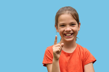 Cheerful White girl in her 10s smiling and pointing up with index finger on blue background. Concept of bright idea, childhood positivity, and educational communication
