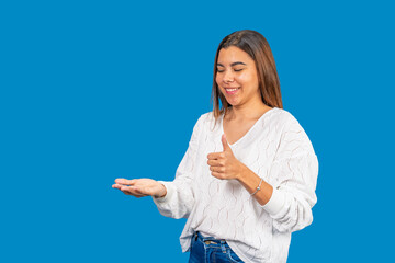 Young woman showing and recommending something with thumbs up on blue background
