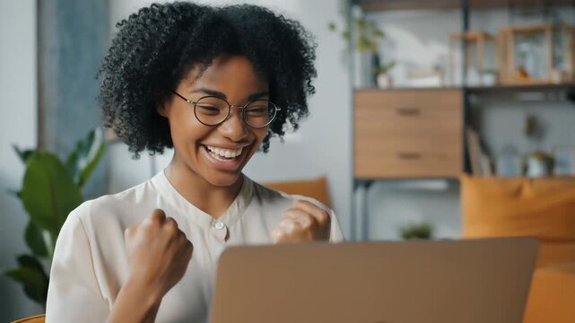 Woman with glasses celebrates success while using laptop in modern office, expressing joy and achievement – Motivates personal growth and success.