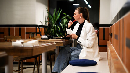 Beautiful woman in a white blazer working on a laptop in a café