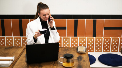Beautiful woman in a white blazer working on a laptop in a café