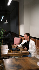 Beautiful woman in a white blazer working on a laptop in a café