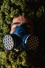 Rare view of man with gas mask covered with weed buds of cannabis