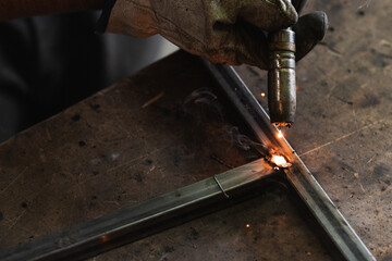 Professional welder welding metal construction parts in industrial workshop. An experienced worker joining iron parts