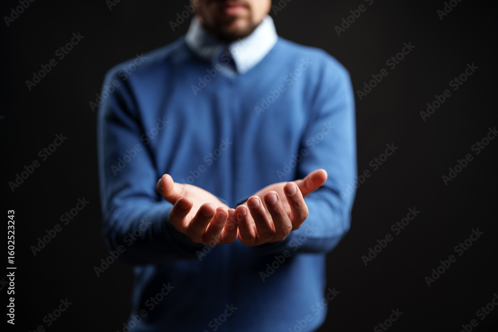 Poster man extending hands in a welcoming gesture against a dark background during a studio session