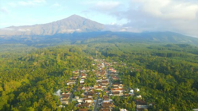 A beautiful village lies peacefully beneath Mount Arjuna, partially obscured by morning clouds.