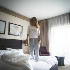 Woman having fun and jumping with bathrobe on bed in hotel room