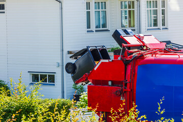Red garbage truck lifting black trash bins for waste collection near residential villas. Sweden.