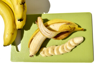 half peeled banana and banana slices on green cut board, top view 