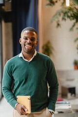 Naklejka premium Smiling black teacher holding notebook in modern classroom