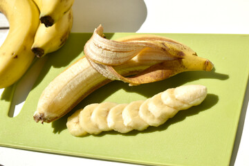 half peeled banana and banana slices on green cut board