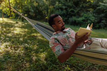 Man lying in a hammock reading a book
