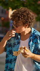 Curly-haired man licking fingers after finishing sandwich in warm sunlight. Concept of street food...