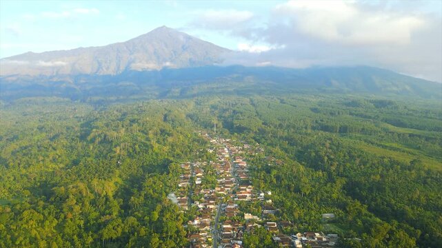A beautiful village lies peacefully beneath Mount Arjuna, partially obscured by morning clouds.