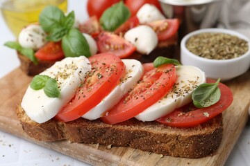 Tasty sandwiches with mozzarella cheese, tomatoes, basil and spices on light table, closeup