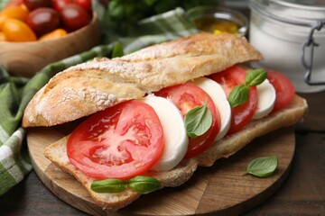 Tasty sandwich with mozzarella cheese, tomatoes and basil on wooden table, closeup