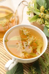 Fresh linden tea in cup, teapot and flowers on white table, closeup