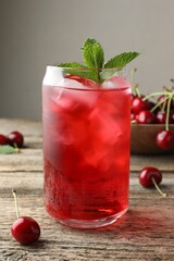 Tasty cherry soda with ice cubes, berries and mint on wooden table, closeup